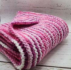 a pink and white crocheted blanket sitting on top of a wooden table next to a fork