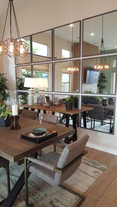 a dining room table and chairs with mirrors on the wall behind them, in front of a large window