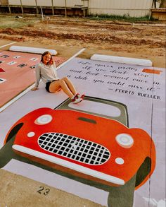 a woman sitting on the ground next to a car painted with words and numbers in front of a building