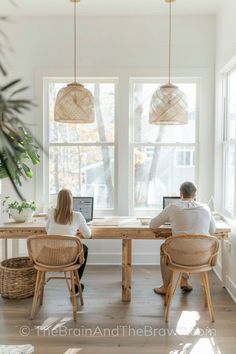 two people sitting at a table with laptops in front of them, looking out the window