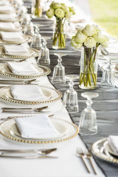 the table is set with silverware and white flowers in glass vases on each side