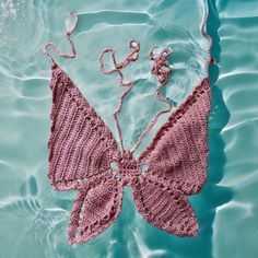 a pink crocheted butterfly laying on top of the water with it's wings spread out