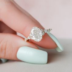 a woman's hand holding a ring with a diamond on it and a white manicure