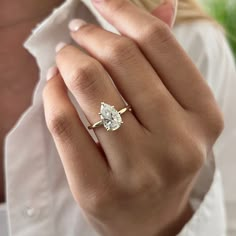 a woman's hand wearing a gold ring with a pear shaped diamond on it