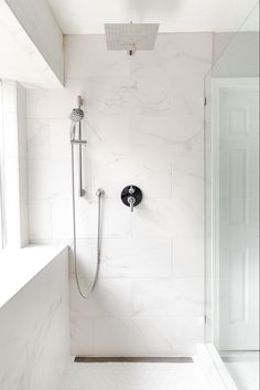 a white bathroom with a shower head and hand held shower faucet in the corner