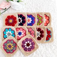 six crocheted coasters are arranged on a white surface with flowers in the background