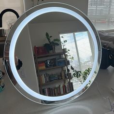 a round mirror sitting on top of a counter next to a book shelf and window