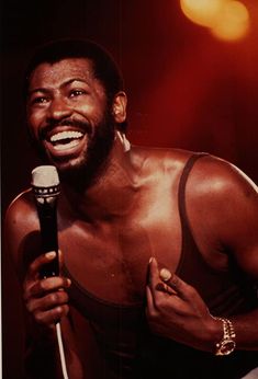 a man holding a microphone in his right hand and smiling at the camera while wearing a tank top