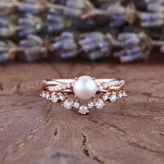 a pearl and diamond ring sitting on top of a piece of wood with flowers in the background