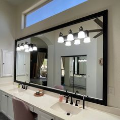 a large bathroom mirror sitting above a white sink under a light mounted on a wall