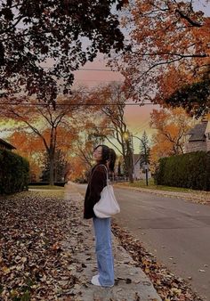 a woman standing on the side of a road with her hand in her pocket and looking up into the sky