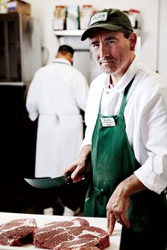 a man in an apron cuts up steak on a cutting board