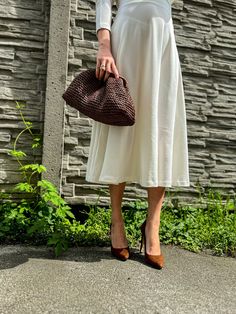 a woman in a white dress holding a brown purse