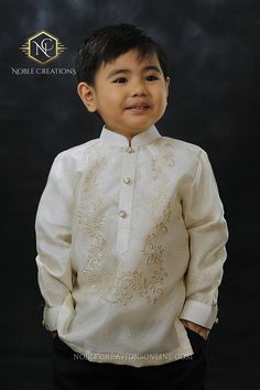 a young boy wearing a white shirt and black pants with gold embroidery on the collar