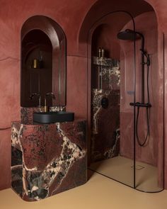 a bathroom with red walls and marble counter tops, along with a black pedestal sink