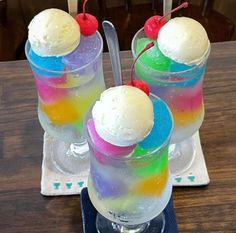 two ice cream sundaes with cherries and rainbow colors on the top, sitting on a table