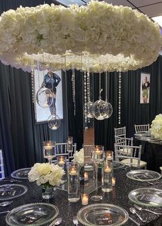 the table is set with clear plates and silverware, white hydrangeas and candles