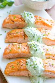 four salmon fillets on a cutting board topped with blue cheese sauce and chives