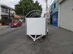 a white box sitting on the side of a road next to a red car and buildings