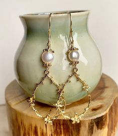 Enhance your boho chic style with this set of long gold teardrop-shaped flower branch dangly earrings. Featuring large gold-plated brass flower branch charms, these earrings are delicately crafted and exude a sweet charm. The handmade earring hooks, crafted with 10K gold-filled wire, add a touch of elegance. At the top, white freshwater pearls with gold-plated floral bead caps provide a classic and timeless accent. Measuring 2 1/2" X 7/8", including the gold-filled wire hooks, these earrings are Delicate Dangle Chandelier Earrings, Delicate Gold Chandelier Earrings With Pearl Drop, Gold Whimsical Flower-shaped Earrings, Gold Flower Chandelier Earrings Elegant Style, Delicate Teardrop Flower Earrings For Pierced Ears, Bohemian Gold Drop Earrings, Gold Flower-shaped Elegant Chandelier Earrings, Delicate Teardrop Flower Earrings, Elegant Gold Flower Chandelier Earrings