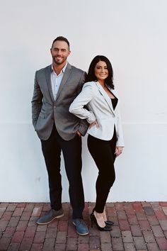 a man and woman standing next to each other in front of a white wall wearing business attire