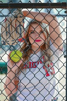 a young woman holding a baseball and glove behind a chain link fence with the ball in her hand