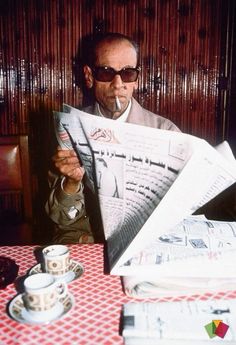 a man sitting at a table with newspapers in front of him and a cup of coffee