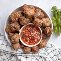 a bowl filled with meatballs covered in marinara sauce next to a basil leaf