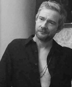 black and white photograph of a man with no shirt looking at the camera while wearing a necklace