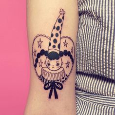 a black and white photo of a clown tattoo on the left inner arm, with stars around it