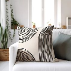 a white couch with pillows on it in front of a potted houseplant