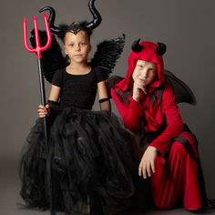 two children dressed up as devil and demon with pitchforkers on their heads, sitting next to each other