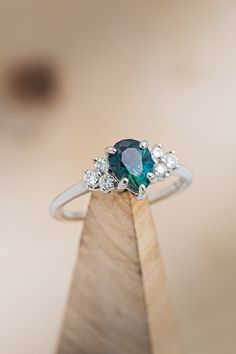 a blue diamond ring sitting on top of a wooden stand with three diamonds around it