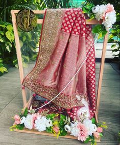 a red and pink saree with flowers on the ground in front of a wooden frame