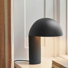 a black lamp sitting on top of a white table next to a book and window