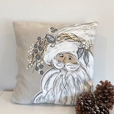 a decorative pillow with an image of a santa clause on it next to a pine cone