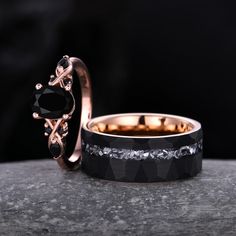 two wedding bands with black diamonds and gold rings on top of each other in front of a dark background