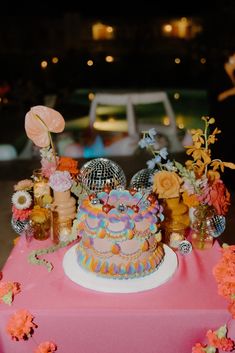 a pink table topped with a colorful cake and lots of flowers on top of it