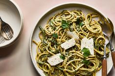 pasta with pesto and parmesan cheese in a white bowl next to silverware