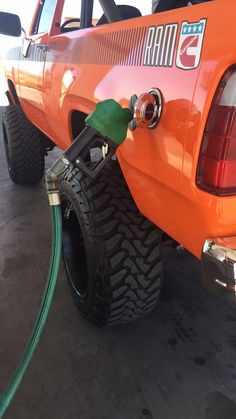 an orange pick up truck with a green hose attached to it's rear end