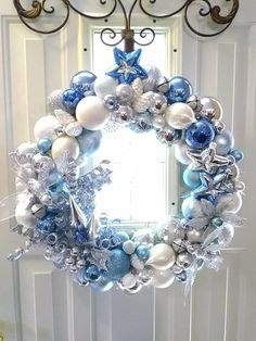 a blue and white christmas wreath hanging on the front door with ornaments around it,