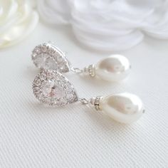 a pair of white pearl and diamond earrings on top of a table next to flowers