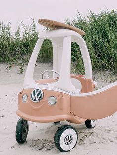 a pink and white toy car sitting on top of a sandy beach next to tall grass