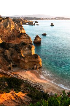 the beach is surrounded by large rocks and cliffs, along with a wooden walkway leading to the water's edge