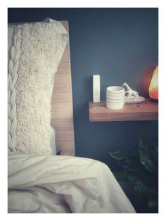 a night stand with two candles and a mug on it next to a bed in a bedroom