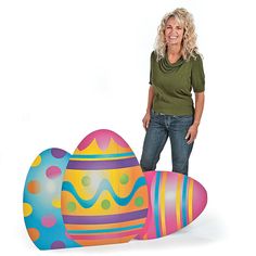 a woman standing next to three decorated eggs