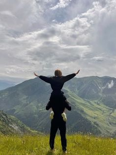 a man and child standing on top of a lush green hillside with mountains in the background