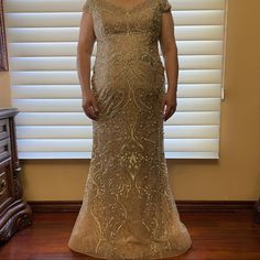 a woman standing in front of a window wearing a gold dress