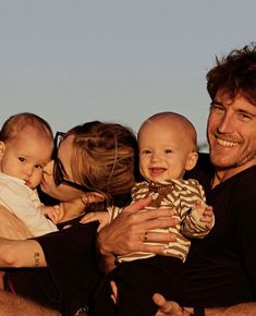 a man is holding two babys and smiling at the camera with his family around him