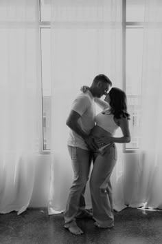 a man and woman standing next to each other in front of a window with curtains